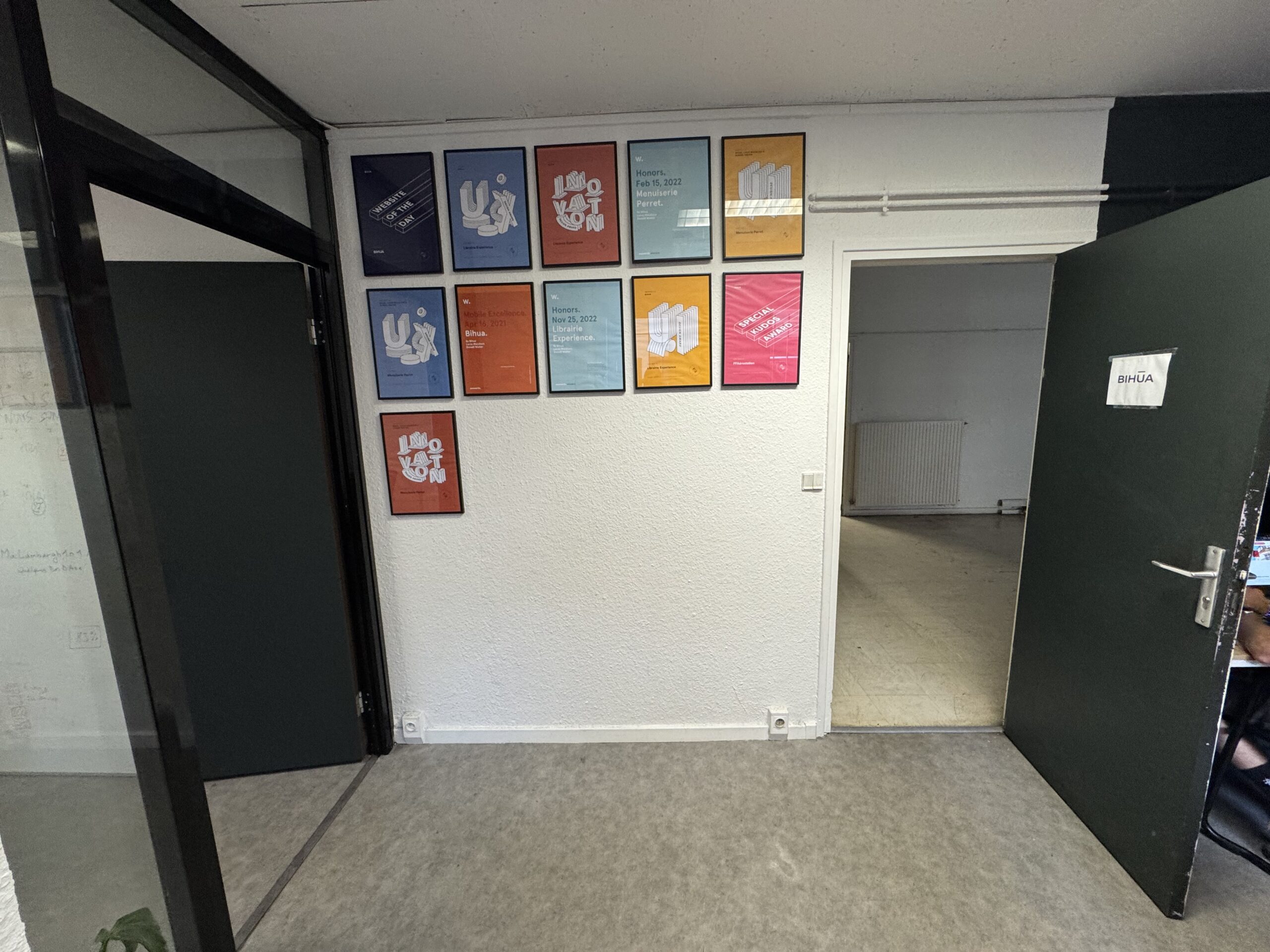 Cadres de créations graphiques sur un mur entre la salle vitrée et l’entrée d’un bureau.